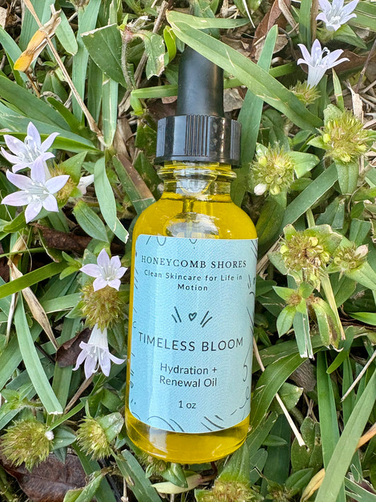 Bottle of 'Timeless Bloom' oil from Honeycomb Shores on grass with flowers